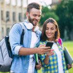 College students smiling, looking at phone on campus
