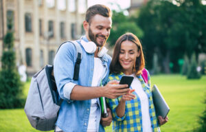 College students smiling, looking at phone on campus