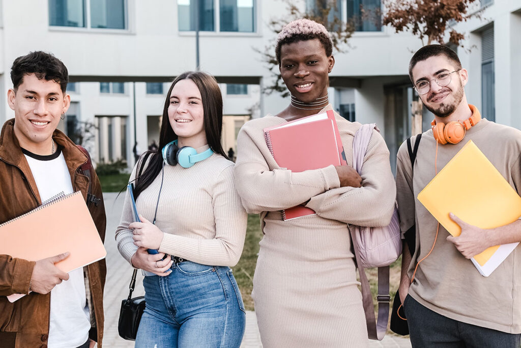 College students outside, smiling and holding books.