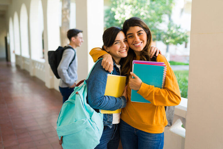 best friends with backpacks and books hugging and smiling while enjoying college together