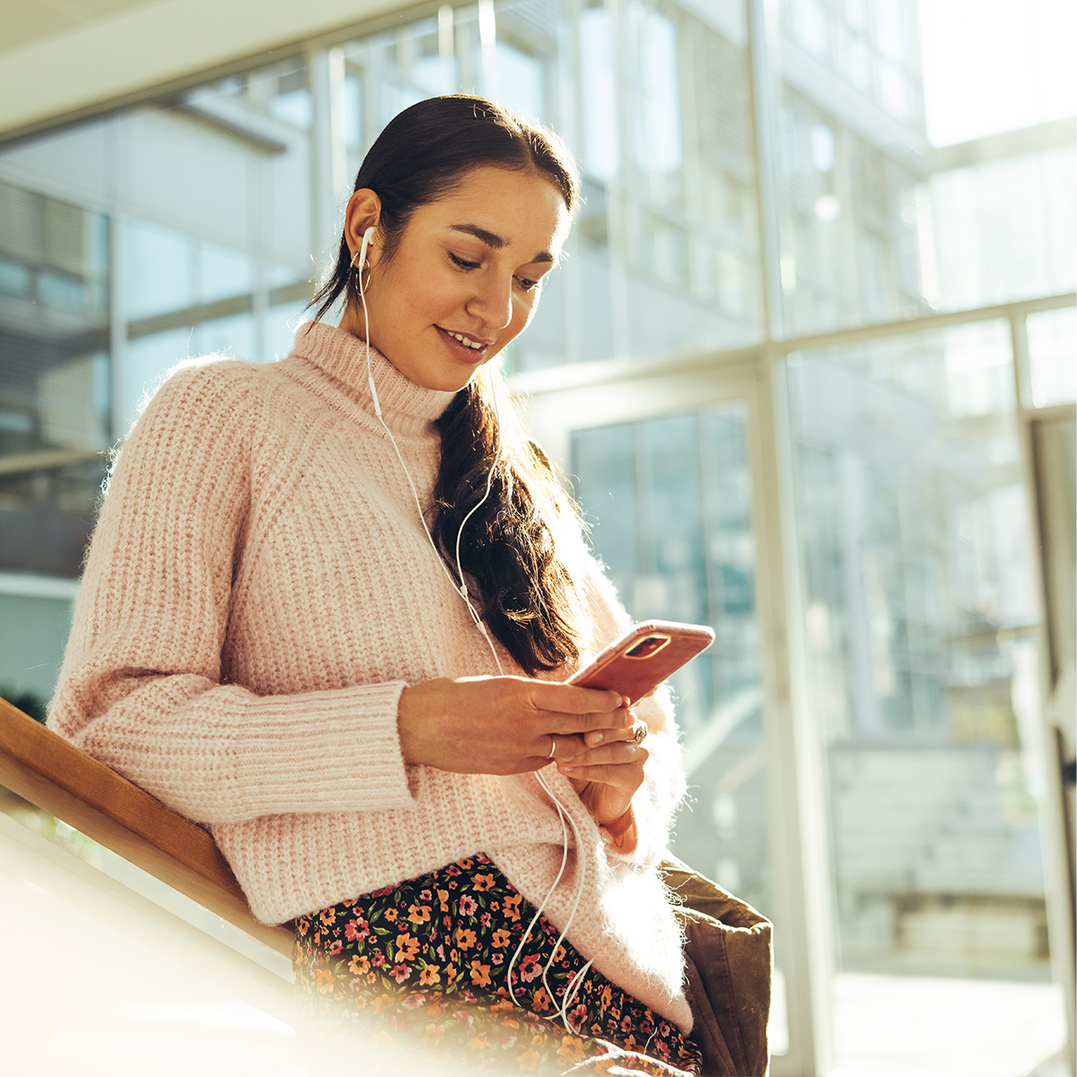 Female student leans on stairwell and looks at her phone.
