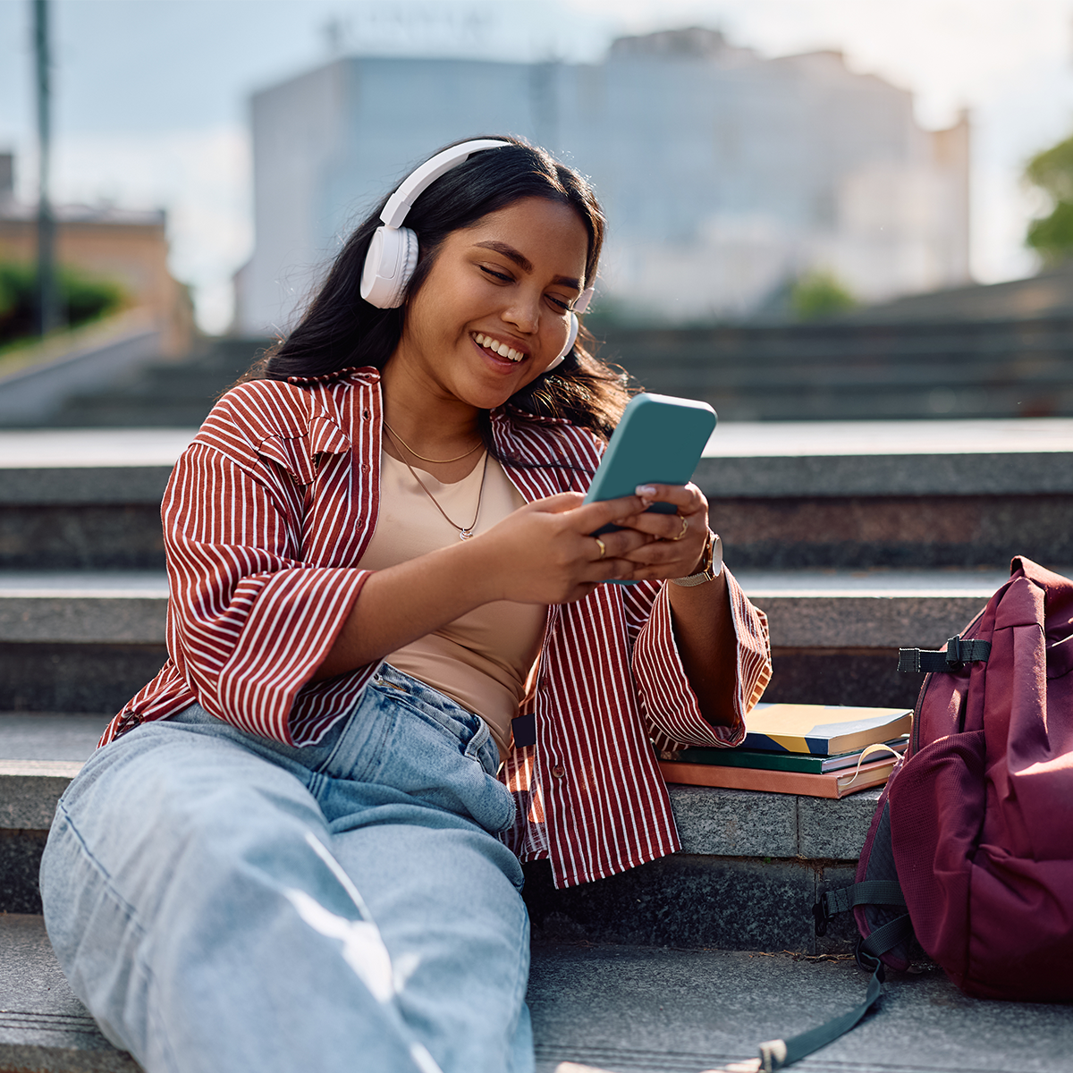 Female student sits outside on campus, smiling and holding her phone.