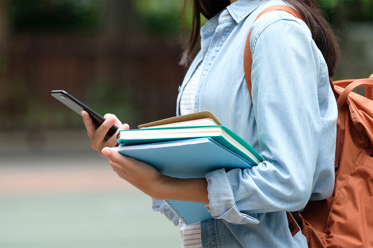 College student on campus with backpack holding a phone