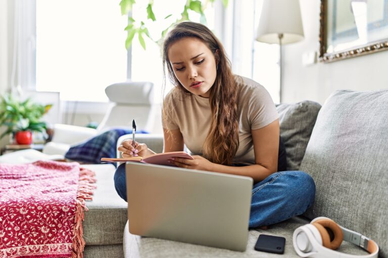 College student writing on notebook on couch