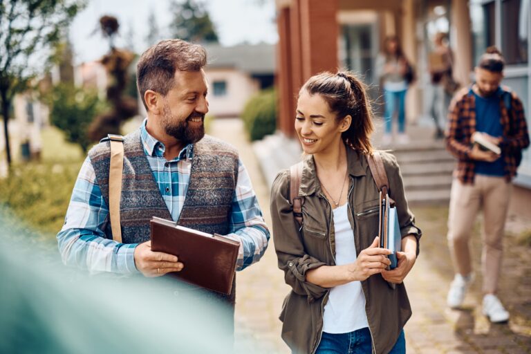 Happy mature student and his younger college friend talking while walking through campus after the lecture.