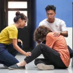 Two students comforting their classmate sitting on the floor in college hallway.