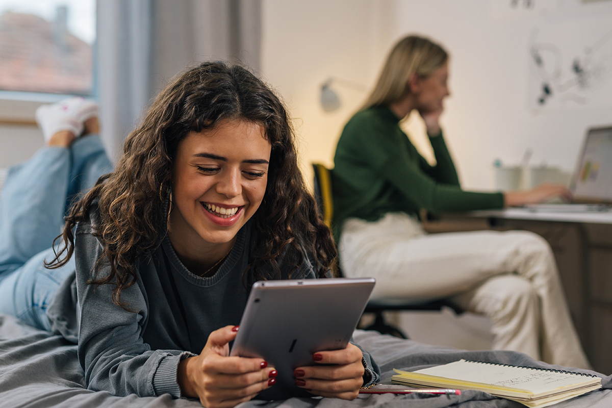 Female college student in residence hall on tablet with roommate