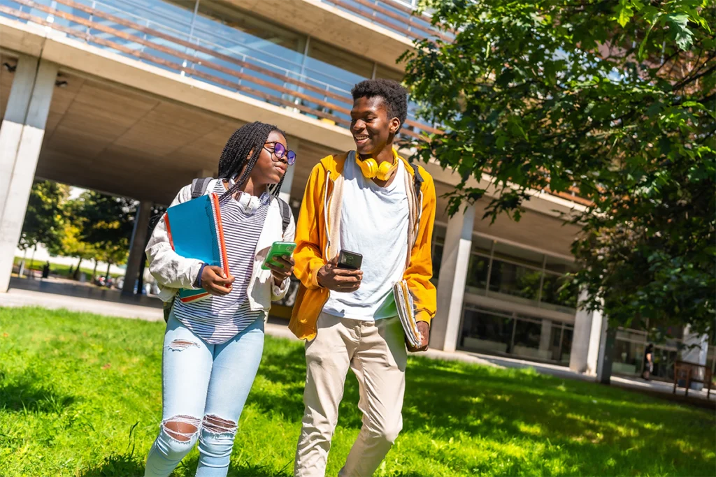 Two African American students walking outside on a college campus with a building behind them