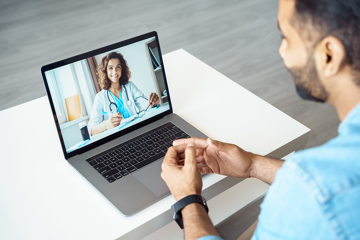 A man sits before an open laptop on a video call with a doctor