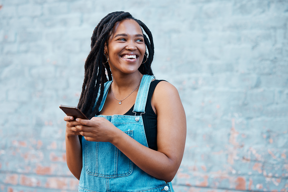 College student holding phone and standing against wall