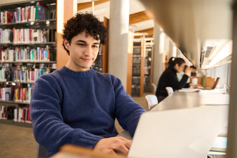Male high school student looking at computer in library