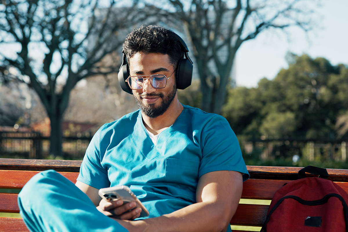 Male medical student sitting on bench looking at phone